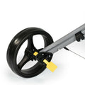 A large black wheel with a sleek design is mounted on a grey frame featuring a yellow brake pedal its design suggests it is part of a wheeled device for movement or transport.