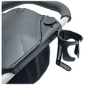 A black stroller accessory attaches to the side holding a cup holder while displaying a textured surface on the main body and a fabric storage compartment below.