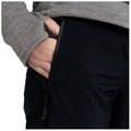 A hand is inserted in the side pocket of black pants while wearing a gray patterned long-sleeve top showcasing a close-up view of clothing and hands without any additional context.