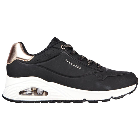 A black athletic shoe with a sleek design features a white midsole and a metallic bronze accent on the heel while displaying the brand name Skechers prominently on the side.