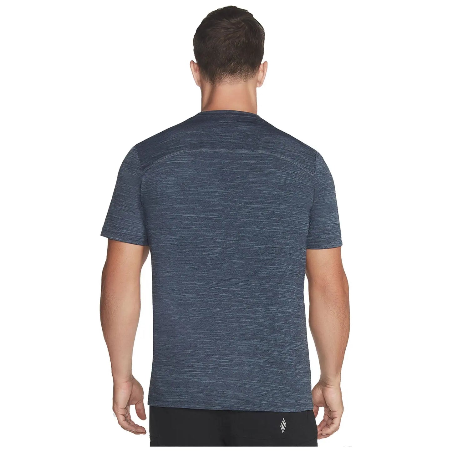 A man is standing with his back facing the viewer wearing a textured navy blue athletic t-shirt in a neutral space emphasizing the shirt's design and fit.