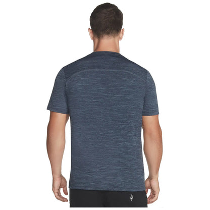 A man is standing with his back facing the viewer wearing a textured navy blue athletic t-shirt in a neutral space emphasizing the shirt's design and fit.