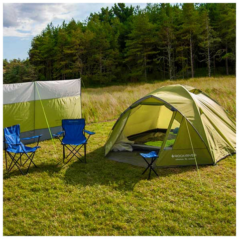 A green tent stands in a grassy area surrounded by trees while two blue folding chairs sit nearby offering a cozy camping setup in a natural outdoor environment.