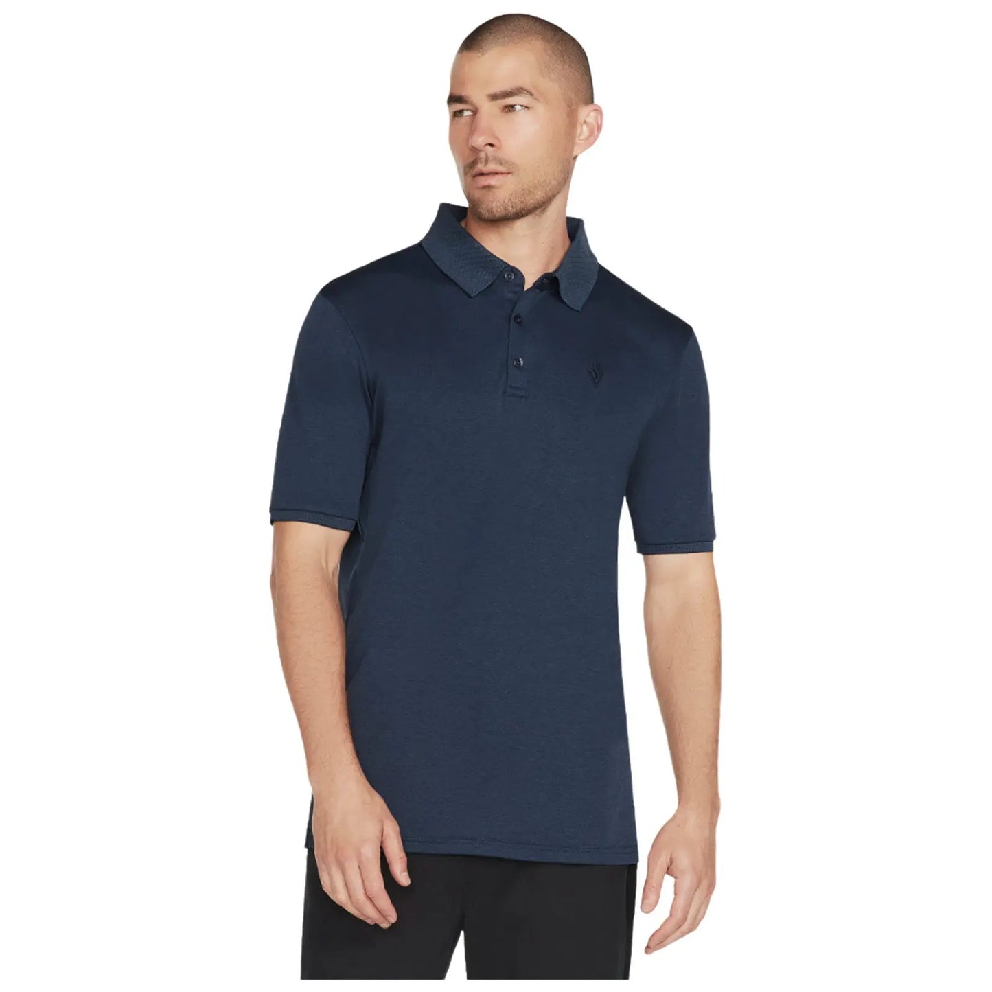 A man stands wearing a navy blue polo shirt with a collar and short sleeves looking slightly to the side in a neutral background suggesting a casual or relaxed setting.