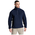A man is standing confidently in a navy fleece pullover with a high collar and buttoned placket wearing light-colored pants in a neutral background.