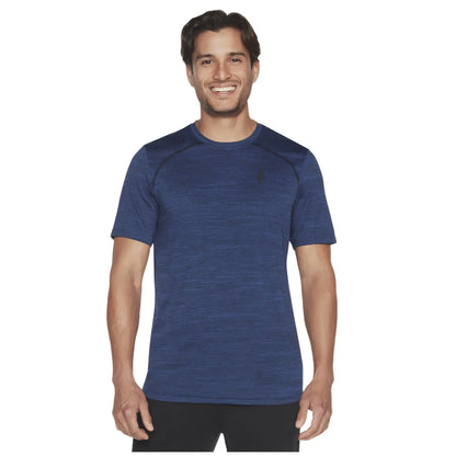 A man is smiling while wearing a blue athletic shirt with short sleeves. He stands against a plain white background, presenting a casual and friendly appearance.