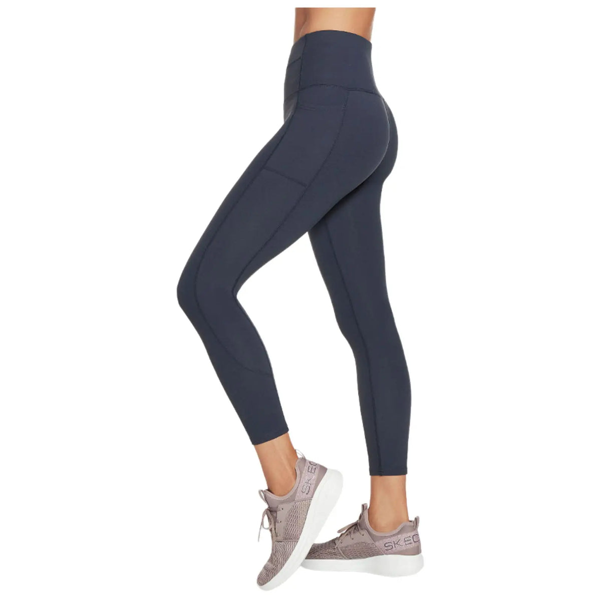 Leggings in a dark tone fit snugly on a model’s legs paired with light athletic sneakers showcasing an activewear style presented against a plain background.