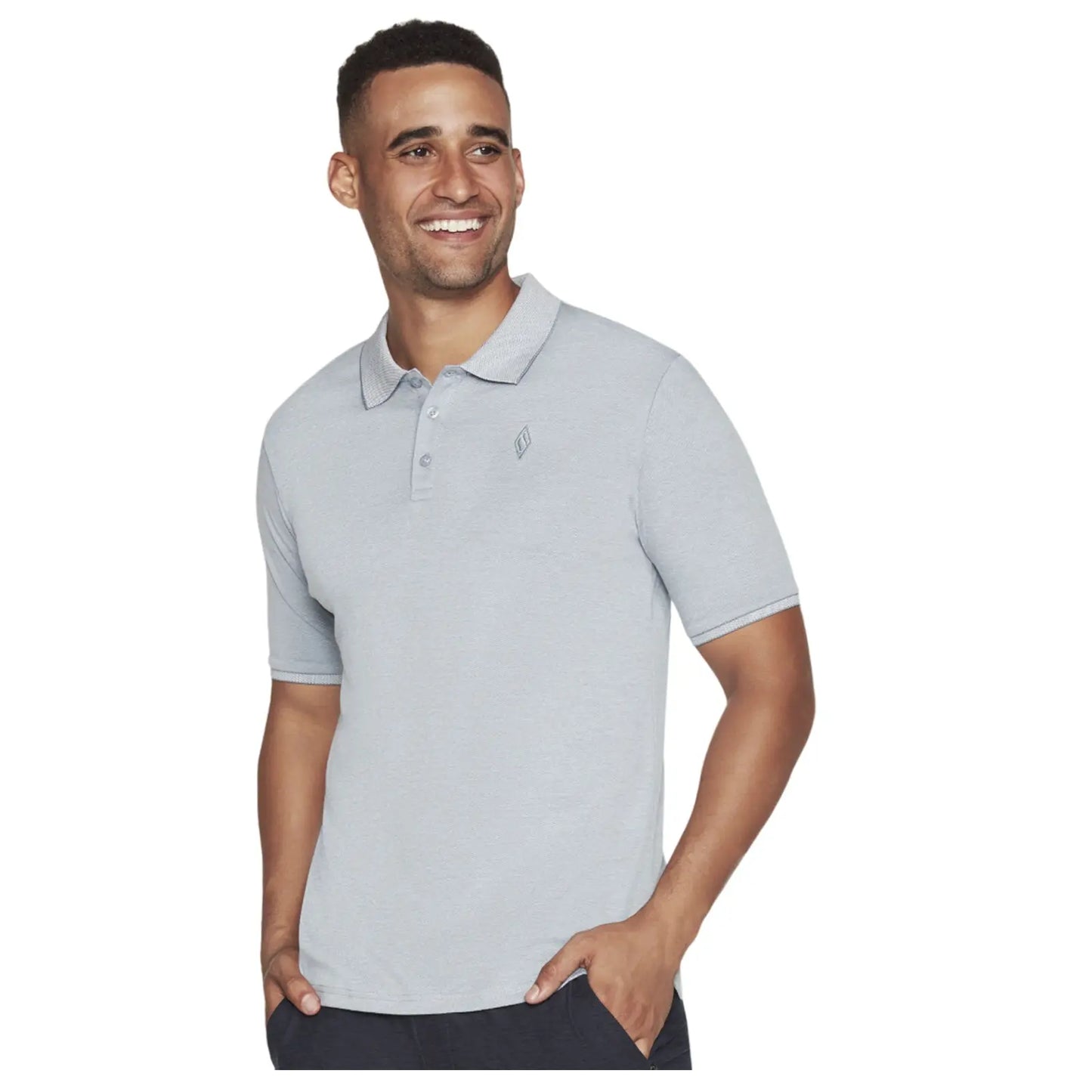 A man wearing a light gray polo shirt smiles while standing with one hand in his pocket against a neutral background. His expression conveys happiness and confidence.