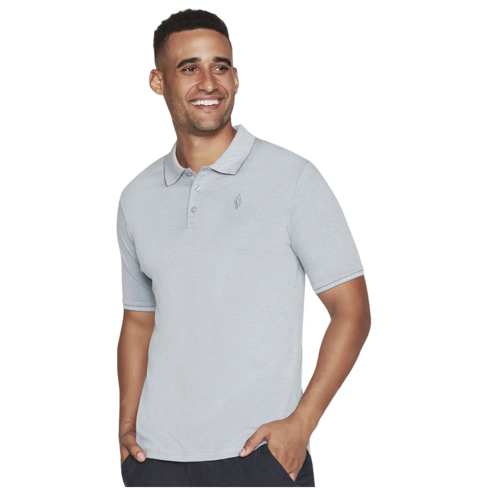 A man wearing a light gray polo shirt smiles while standing with one hand in his pocket against a neutral background. His expression conveys happiness and confidence.