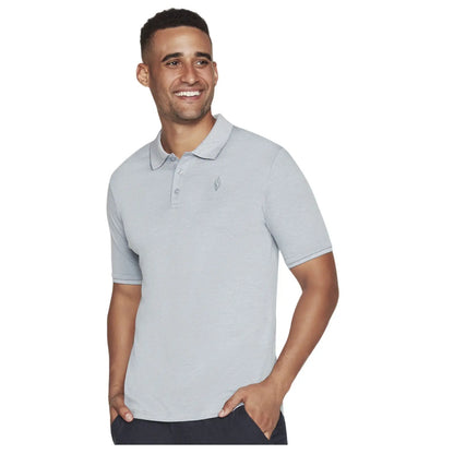 A man wearing a light gray polo shirt smiles while standing with one hand in his pocket against a neutral background. His expression conveys happiness and confidence.