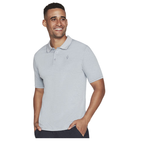 A man wearing a light gray polo shirt smiles while standing with one hand in his pocket against a neutral background. His expression conveys happiness and confidence.