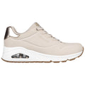 A beige sneaker with a metallic gold accent is displayed side-on featuring perforations on the upper part and a visible air cushioning unit in the white midsole