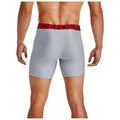 A person is standing with their back to the viewer wearing gray boxer briefs with a red waistband displaying the word "UNDERARMOUR" in bold letters. The setting is neutral, focusing on the apparel.