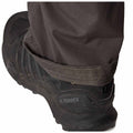 A black hiking shoe is displayed with a dark pant leg partially covering it indicating the person is standing or walking outdoors potentially in a rugged environment.