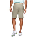 A person is standing with their back facing the viewer wearing tan shorts and a light blue shirt showing athletic footwear with green accents in a neutral environment.