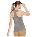 A woman in a gray athletic tank top is seen from behind adjusting her hair with one hand while lightly touching her forehead with the other in a neutral background.