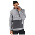 A young man is wearing a light gray hooded sweatshirt with a darker gray pocket while posing and lightly touching his neckline in a neutral background.