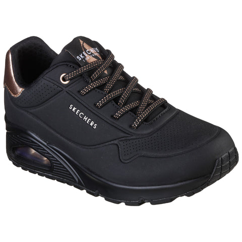 A black sneaker with a textured surface features bronze accents and laces. It showcases a cushioned sole and is designed for comfort and casual wear. The brand name is visible on the side.