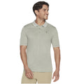 A man is standing and smiling while wearing a light grey polo shirt with a collar and three buttons, complemented by khaki pants, in a neutral background.