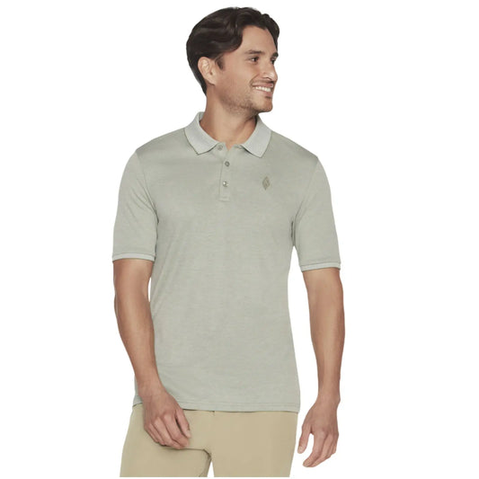 A man is standing and smiling while wearing a light grey polo shirt with a collar and three buttons, complemented by khaki pants, in a neutral background.