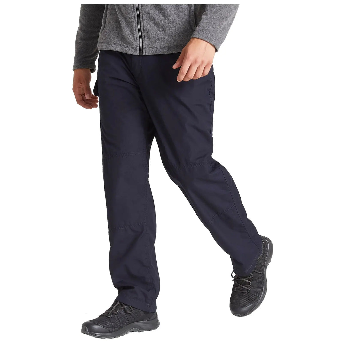 A person is walking in dark pants and a gray zippered jacket wearing black shoes in a neutral, indoor setting. The focus is on their midsection and lower body.
