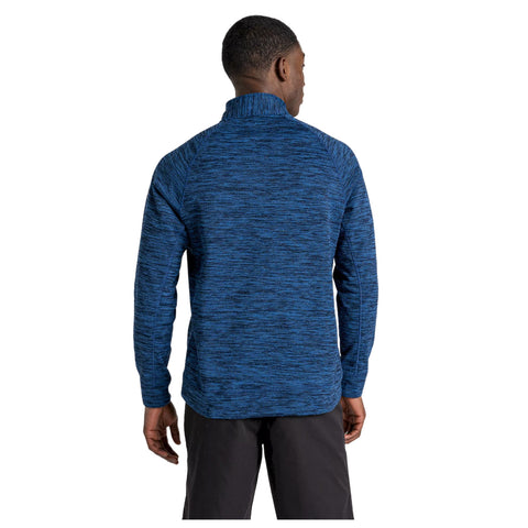 A man wearing a navy blue pullover stands with his back facing the viewer in a neutral environment, showcasing the garment's collar and texture while wearing khaki pants.