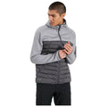 A young man is standing and adjusting a zippered hooded jacket that has a gray textured upper and a puffy gray lower section while wearing dark pants.