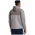 A person is wearing a grey and light grey hooded jacket with a textured design standing with their back facing the viewer in a neutral background environment.