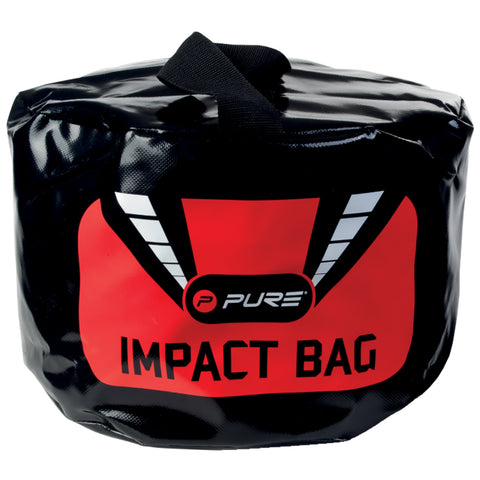 A round black impact bag with a bright red and black design is positioned upright. It features a carrying handle on top and prominently displays the words "PURE IMPACT BAG."