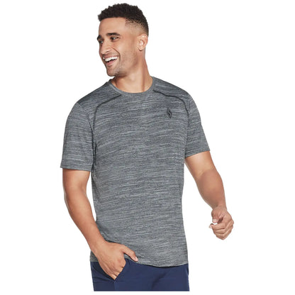A man wearing a gray athletic shirt smiles and appears to be walking in a casual setting with a joyful demeanor and body language that suggests happiness and confidence.