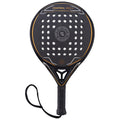 A padel racket with a round shape features a textured black surface dotted with holes and an orange outline alongside a black grip and wrist strap designed for controlled play in sports contexts.
