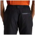 Black trousers are worn with an elastic waistband featuring a small pocket and logo on the back. An orange shirt is visible above, set against a neutral background.