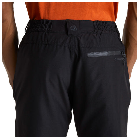 Black trousers are worn with an elastic waistband featuring a small pocket and logo on the back. An orange shirt is visible above, set against a neutral background.