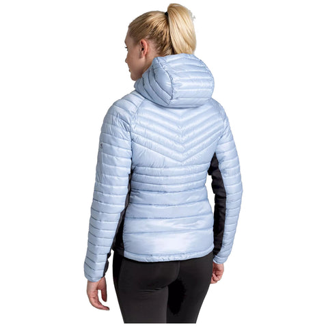 A woman stands facing away wearing a light blue padded jacket with a hood and black sleeves her hair is tied back in a ponytail the background is plain white.