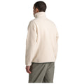 A person wears a cream-colored fleece jacket with a high collar facing away while standing against a plain white background, suggesting a casual setting or fashion display.