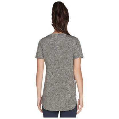 A person is standing with their back facing the viewer wearing a loose-fitting gray short-sleeve shirt that has a rounded hem in a neutral background.