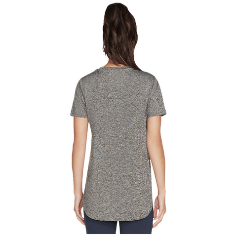 A person is standing with their back facing the viewer wearing a loose-fitting gray short-sleeve shirt that has a rounded hem in a neutral background.