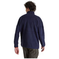 A person wearing a dark navy fleece jacket is seen from the back walking away in a light background with their left hand relaxed at their side and right arm slightly bent.