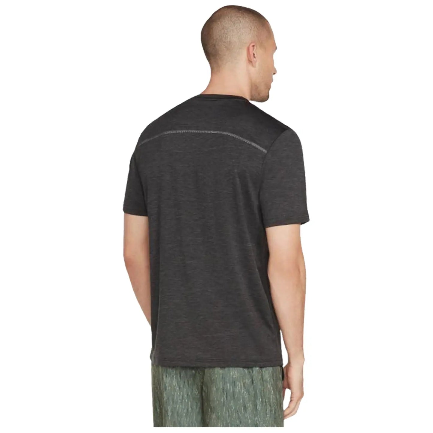 A man is seen from behind wearing a dark grey shirt and light patterned shorts standing in a neutral setting with no distinct features or objects in the background.