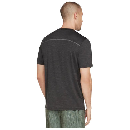 A man is seen from behind wearing a dark grey shirt and light patterned shorts standing in a neutral setting with no distinct features or objects in the background.