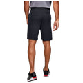 A man is standing with his back to the viewer wearing black shorts and a gray shirt while resting his right hand on his hip in a neutral setting.