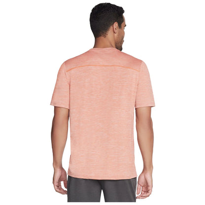 A man is wearing a light orange athletic shirt and gray shorts while standing with his back facing the viewer in a neutral setting without any specific background elements.