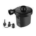 A compact black electric air pump is positioned upright with multiple nozzle attachments nearby intended for inflating items in a household or outdoor setting.