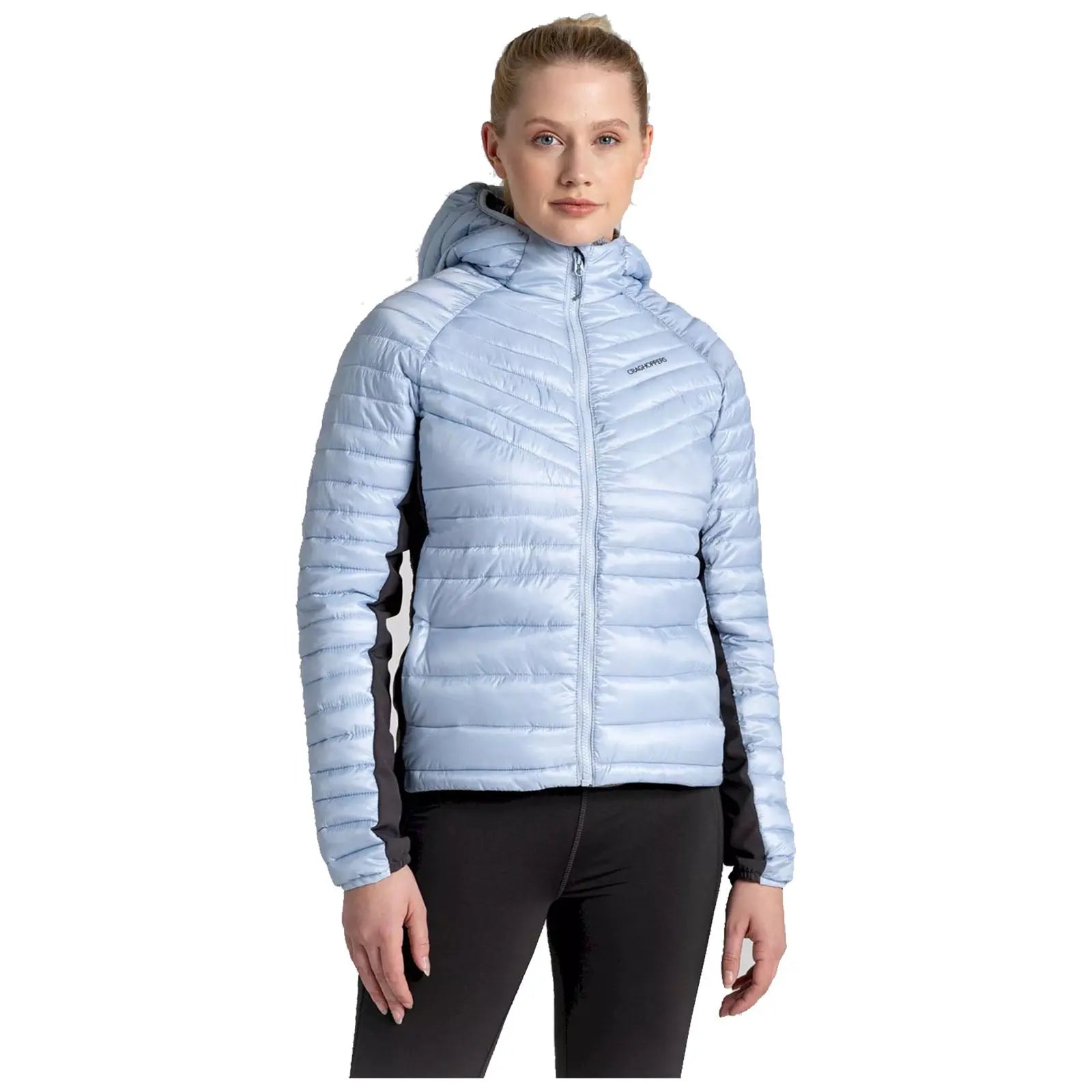 A woman is wearing a light blue puffy jacket with a hood and black accents standing confidently with her hands relaxed at her sides in a neutral setting.