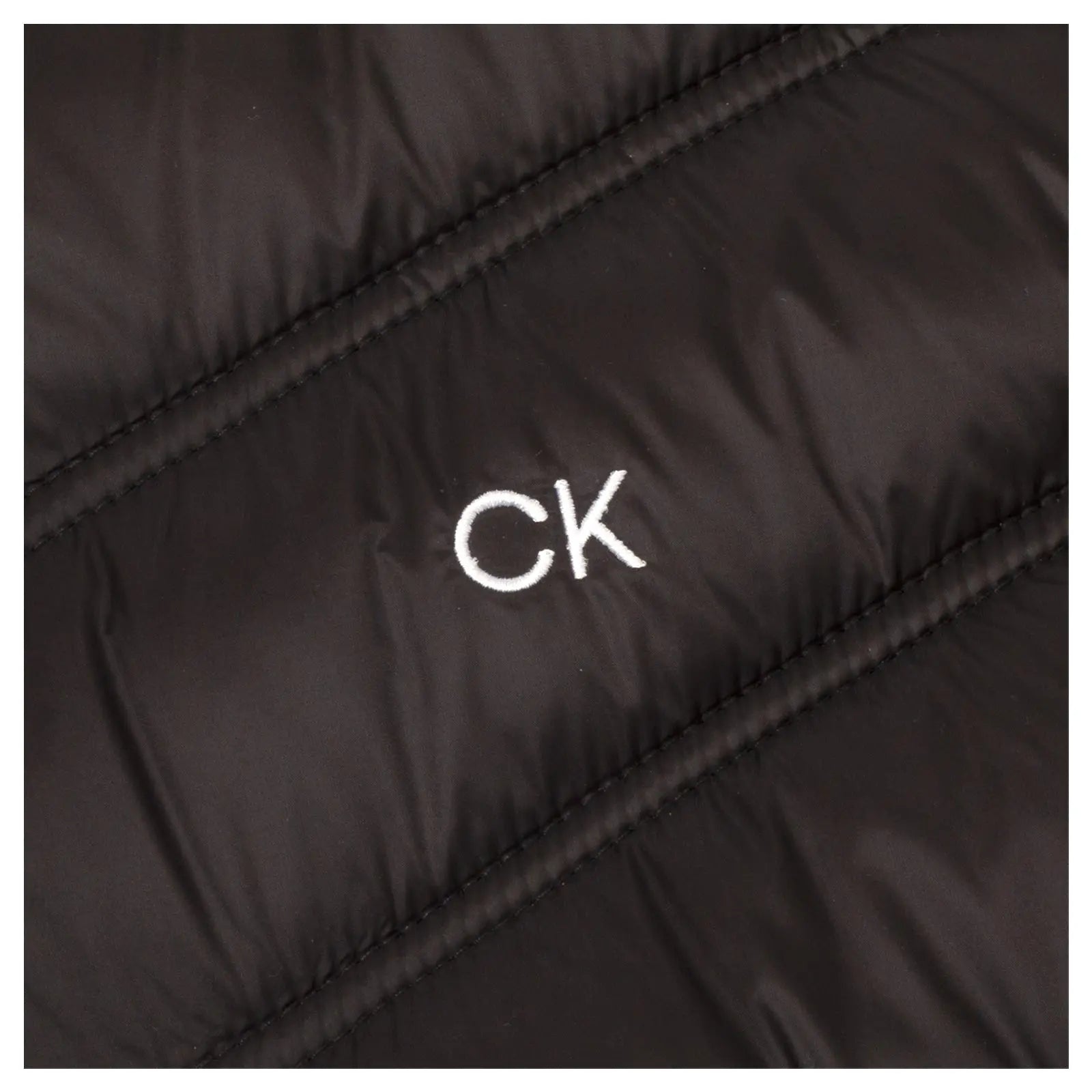 A black puffer jacket is vertically textured with a white "CK" logo prominently displayed on the fabric emphasizing its branding in a close-up view.