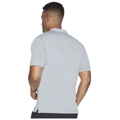 A man stands with his back to the viewer wearing a light gray polo shirt. He has short curly hair and muscular arms, suggesting a casual outdoor setting.