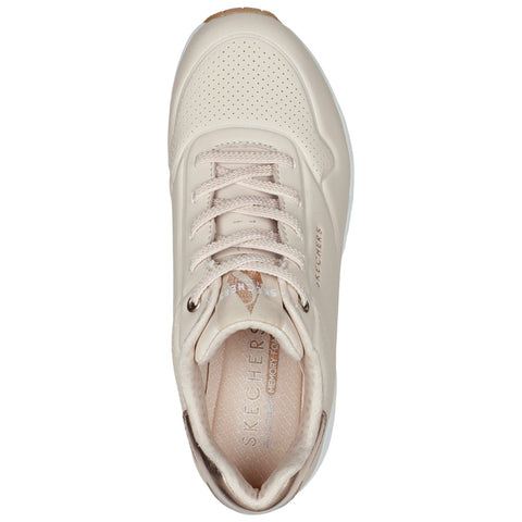 A light beige sneaker with a textured surface displays a lace-up design and a cushioned insole featuring the brand name Skechers prominently embossed on it.