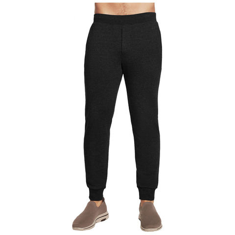 Black jogger pants are being worn by a person standing upright their upper body is not visible the pants fit snugly at the waist and cuffs in a casual setting with casual footwear.