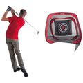 A golfer in a red shirt swings a club to hit a golf ball towards a large practice net with a target in the center set up nearby.