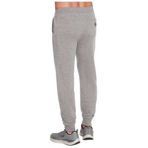 Grey sweatpants are worn by a person standing with their back towards the viewer wearing grey athletic shoes in a neutral indoor setting. A small pocket is visible on the back of the pants.